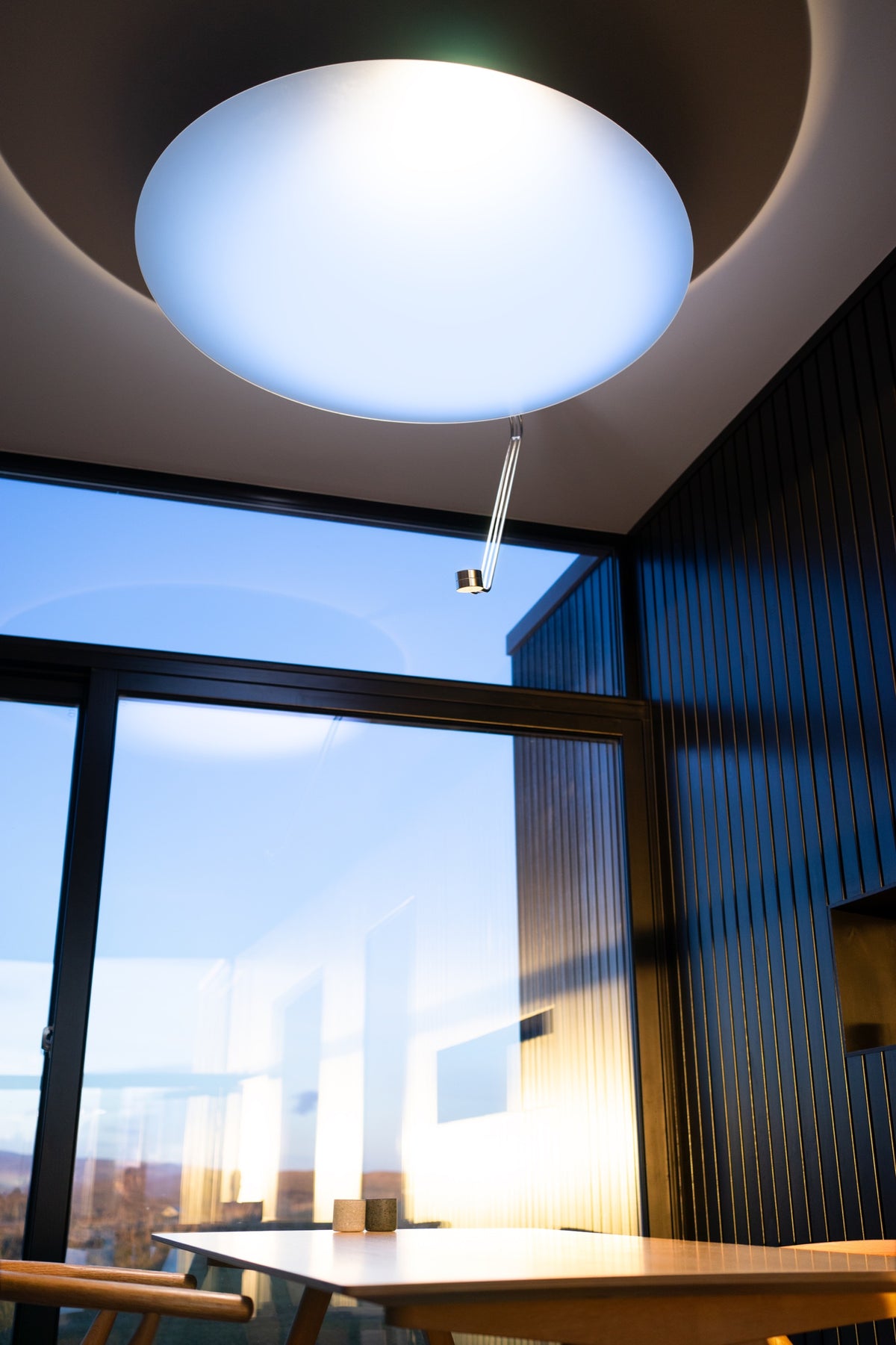 Modern ceiling light fixture in a room with large windows and a view of the city.