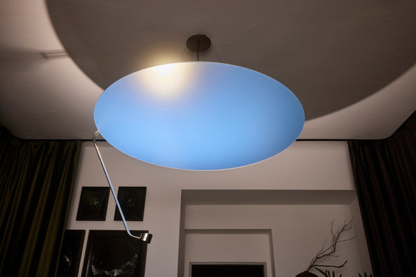 Sunday Light glowing blue overhead in a dark room with curtains and framed pictures