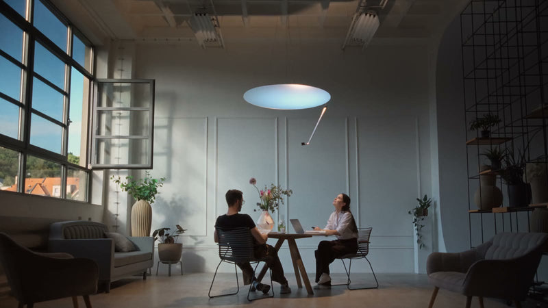 Two people working at a table under Sunday Light in a white room