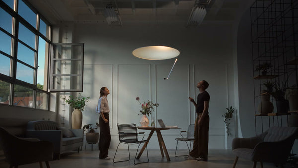 Two people looking up at Sunday Light in a tall room with large windows